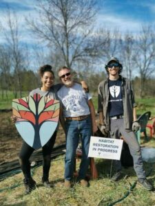 Patricia Wilson, David Marshall, Hayden Wilson at Dance Nature Sanctuary. There is a sign that says "Habitat Restoration in Progress"