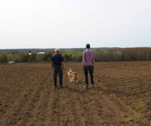 Bruce Kidd and Thom Unrau standing in a field at Kidd Farm in Duoro